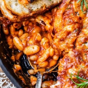 metal spoon and sourdough slice stuck into a cast iron skillet of cheesy beans.