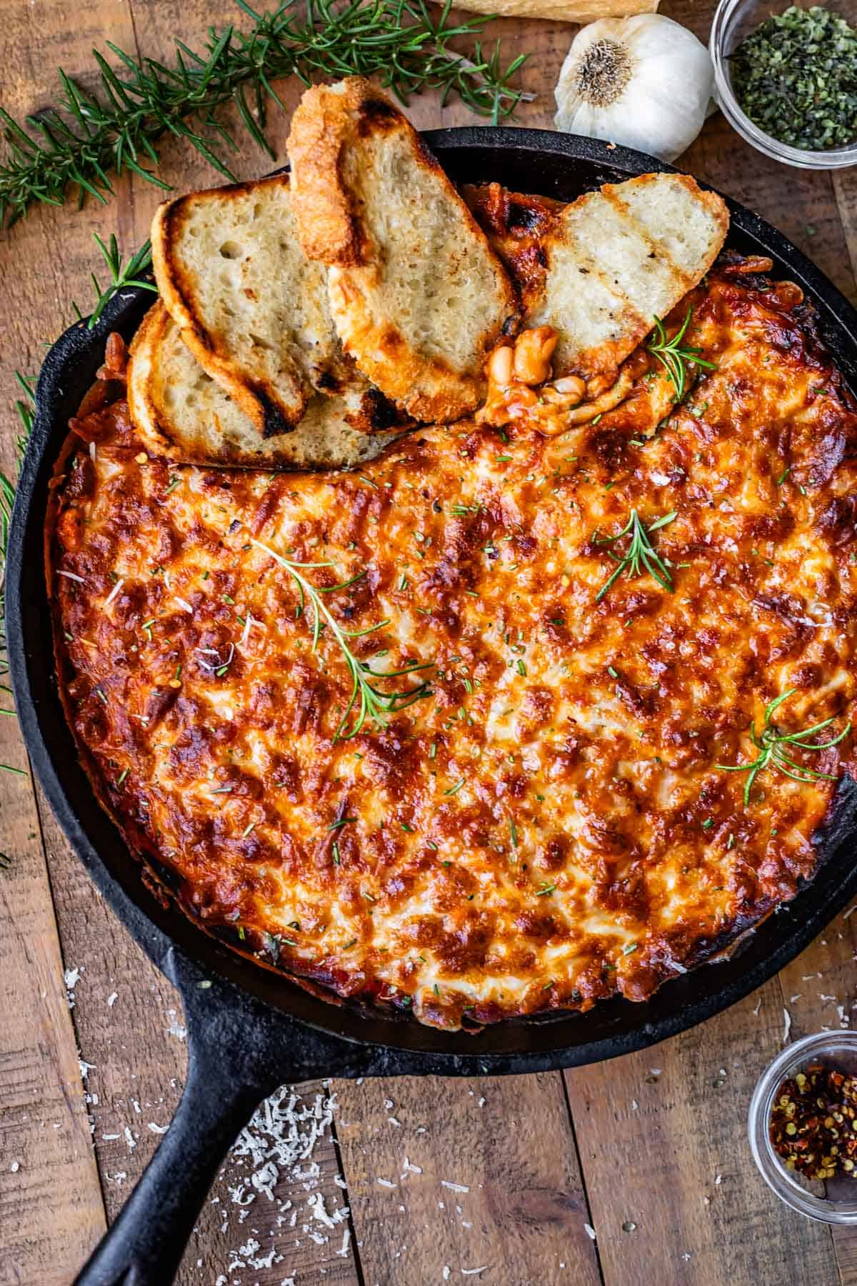 cast iron skillet on a table filled with beans and browned cheese, with sourdough slices in it.