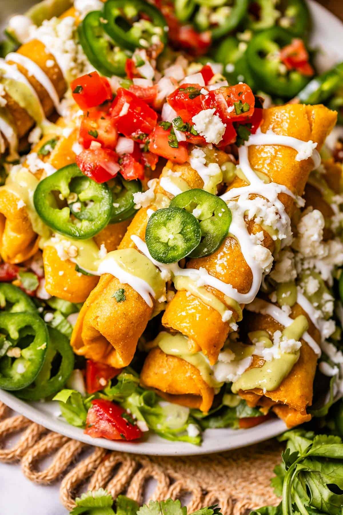 chicken taquitos on a plate garnished with crema, pico de gallo, and jalapenos.