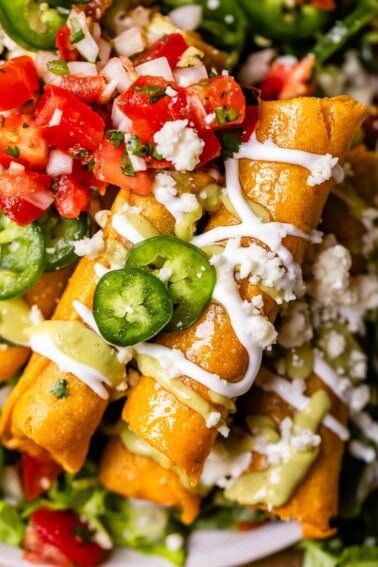 looking straight down at two flautas stacked on top of others, with lots of yummy garnishes.