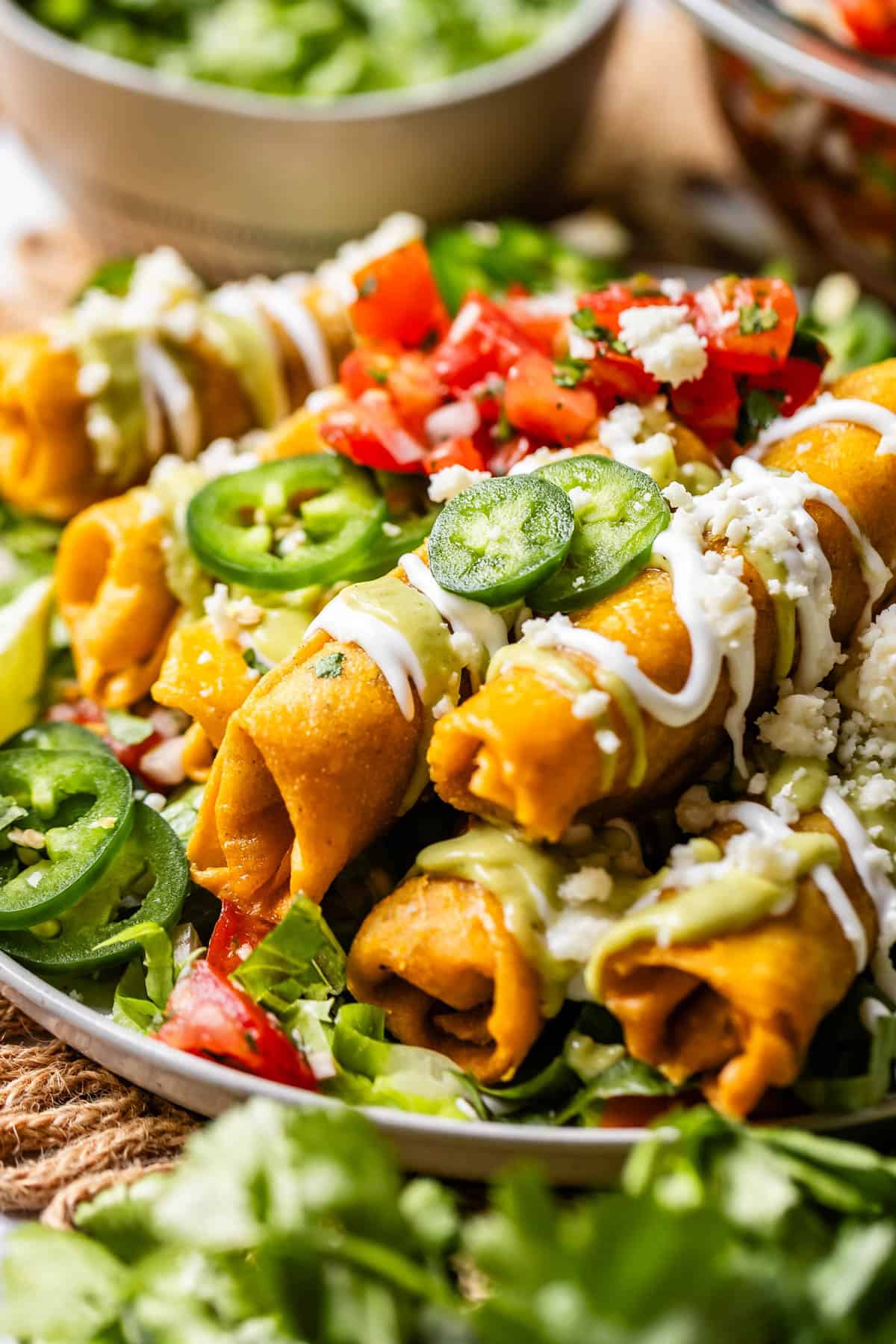 side view of chicken flautas on a plate garnished with jalapenos, pico de gallo, and mexican crema.