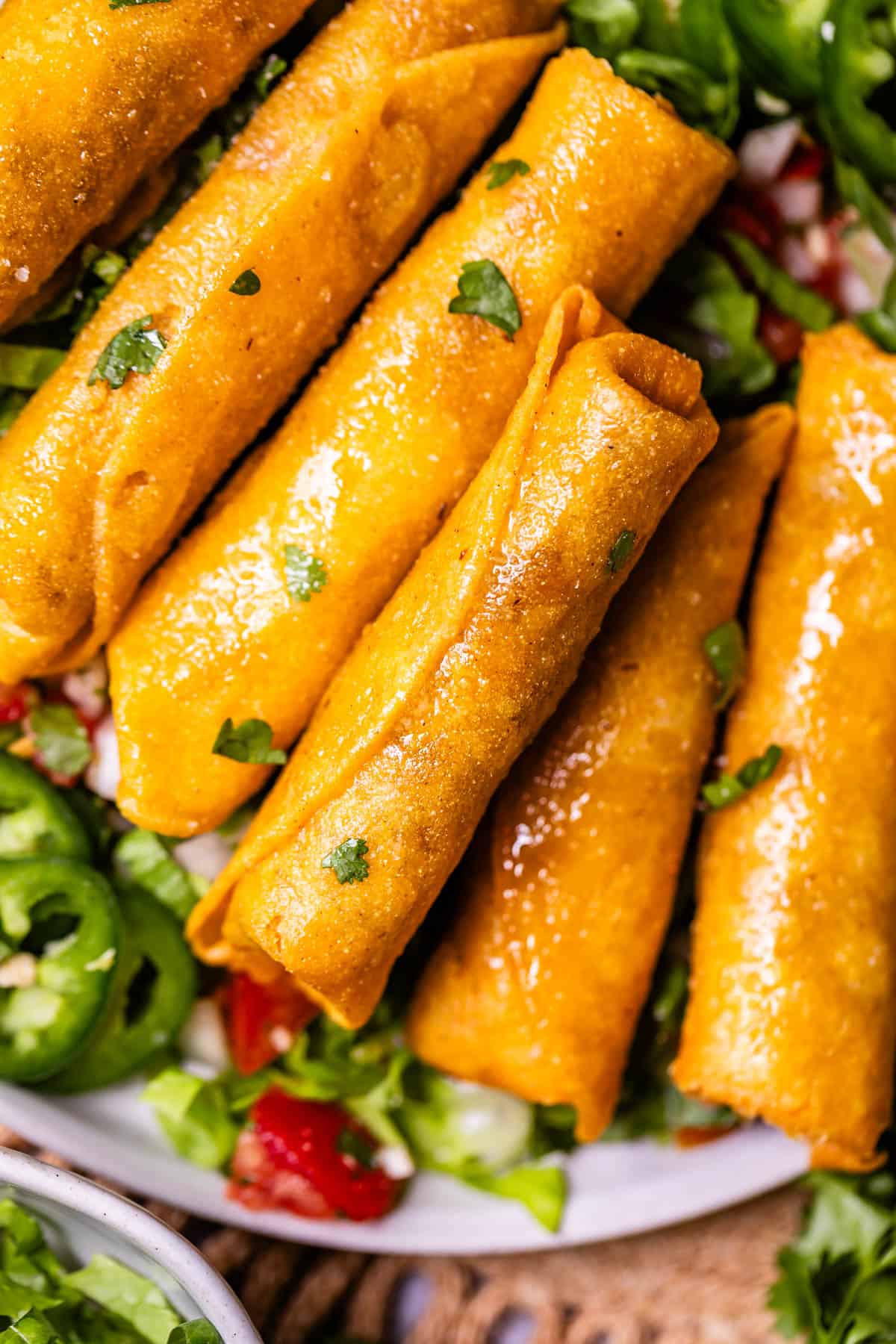 several fried chicken flautas on a bed of lettuce, pico de gallo, and more on a plate.