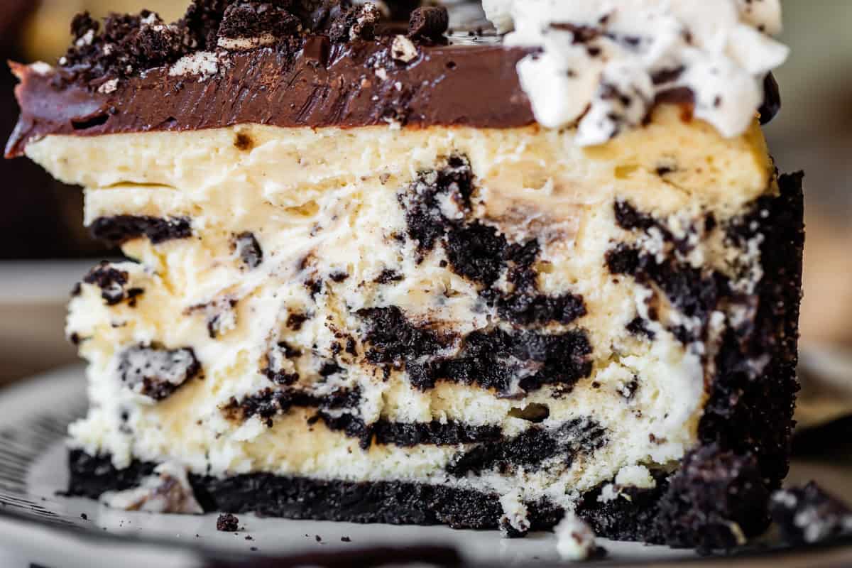 side view of a tall slice of oreo cheesecake with oreo crust, ganache, and whipped cream.
