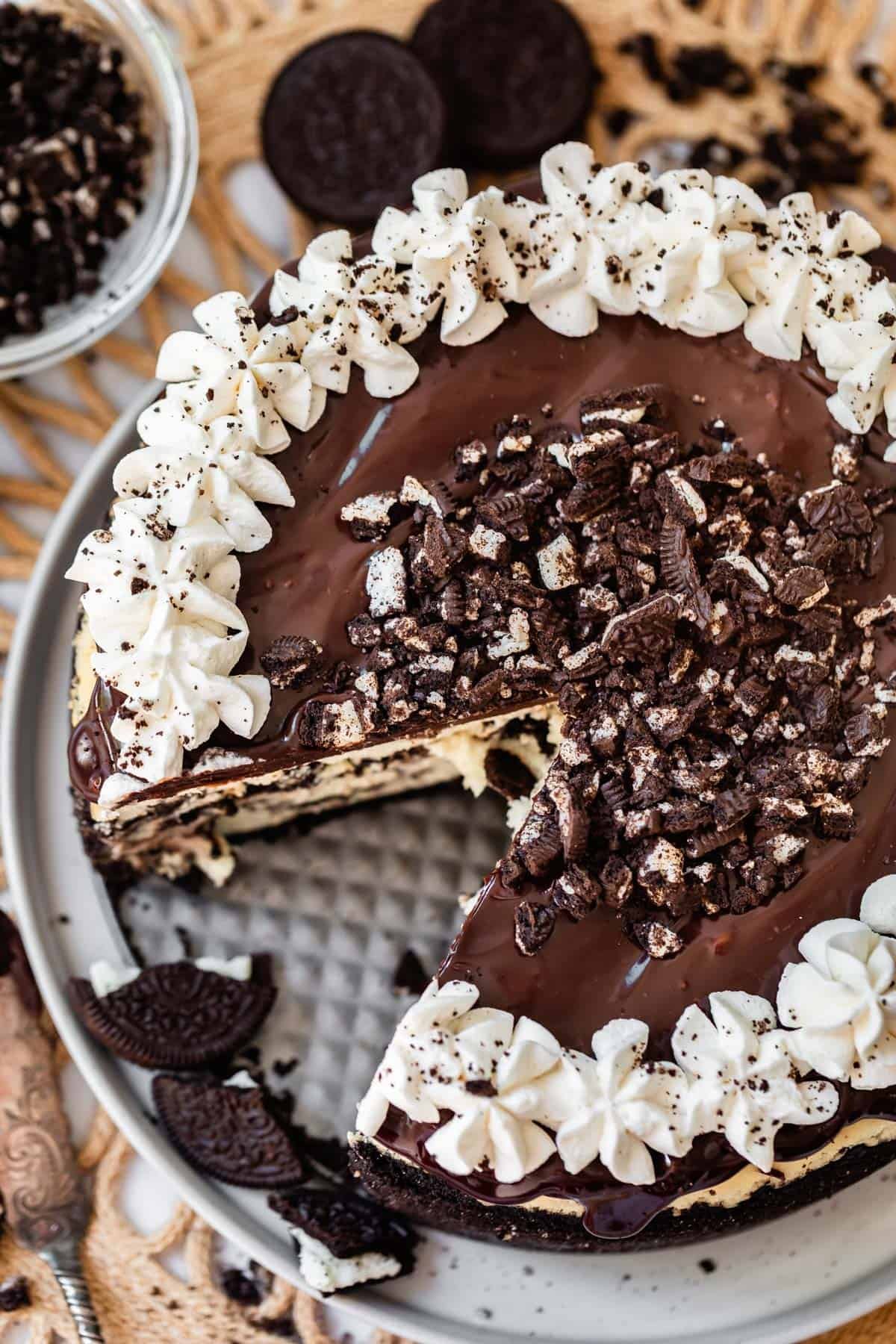 top view of a ganache & oreo topped oreo cheesecake with oreo crust with a slice removed.