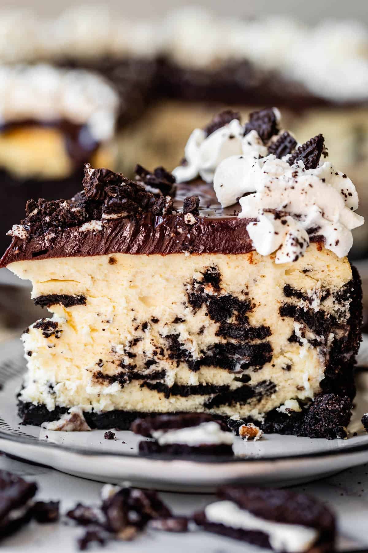 side view of a tall slice of oreo cheesecake with oreo crust, ganache, and whipped cream.