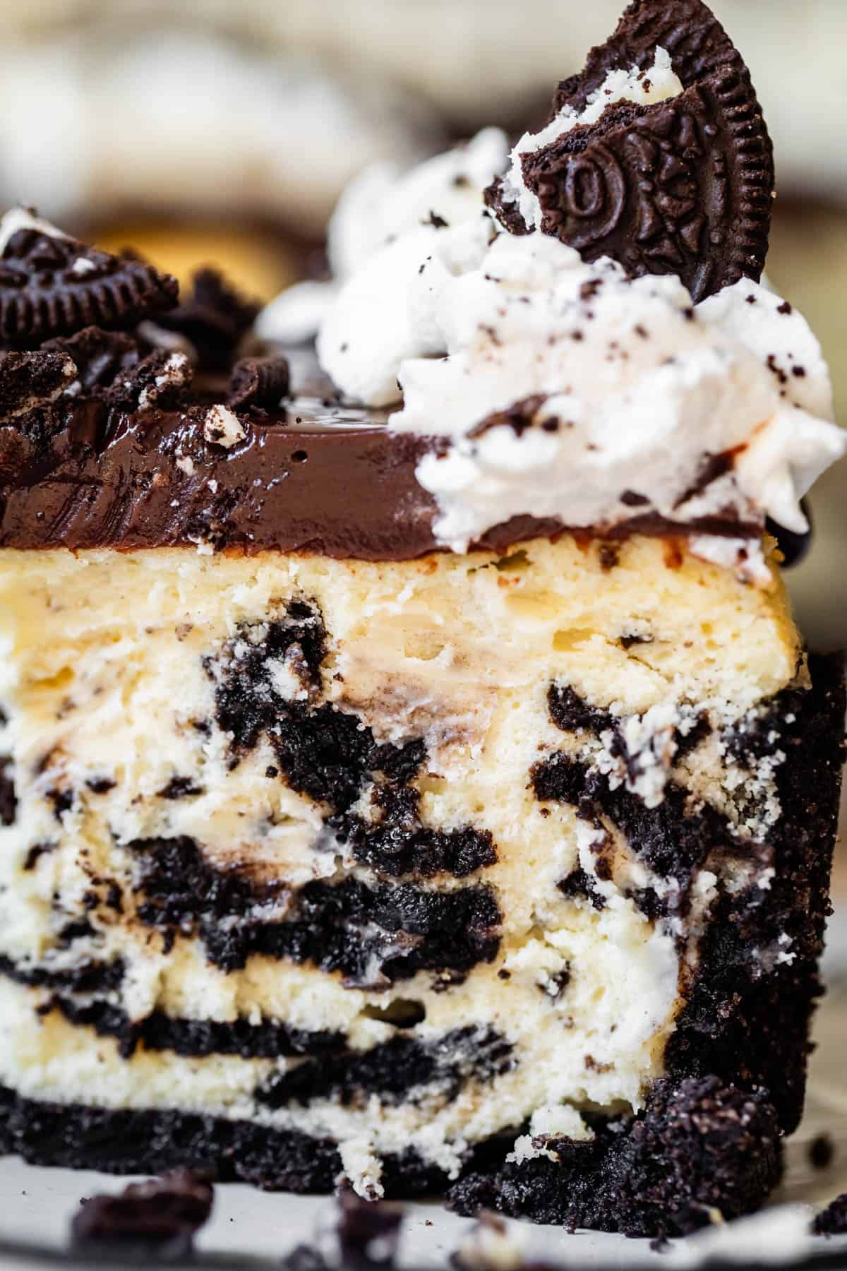 side view of a tall slice of oreo cheesecake with oreo crust, ganache, and whipped cream.
