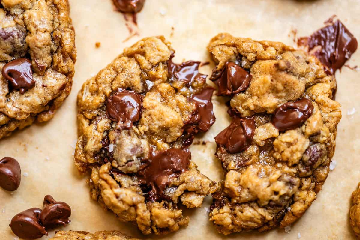 close up of an oatmeal chocolate chip cookie with melty chips on parchment paper.