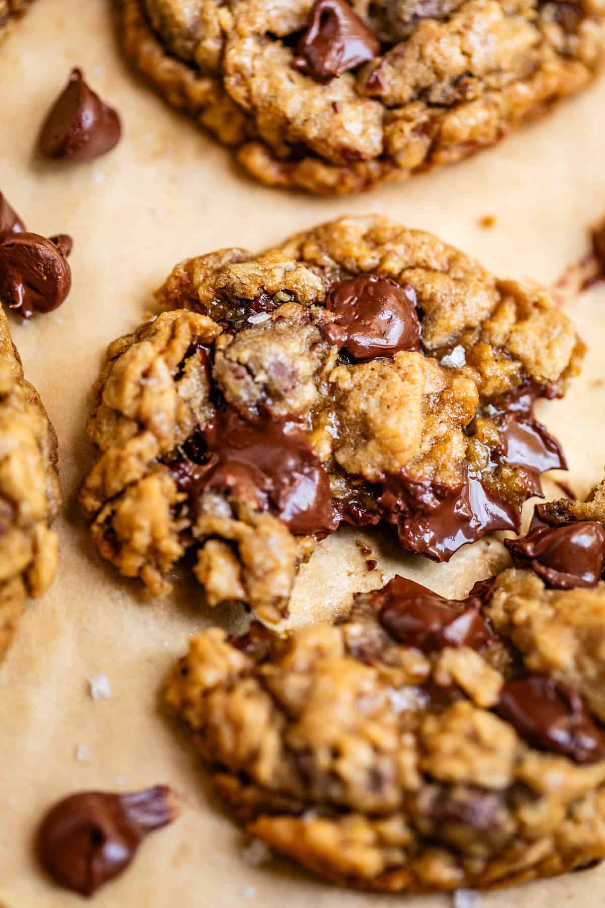 oatmeal chocolate chip cookie with melty chocolate split in half on parchment paper.