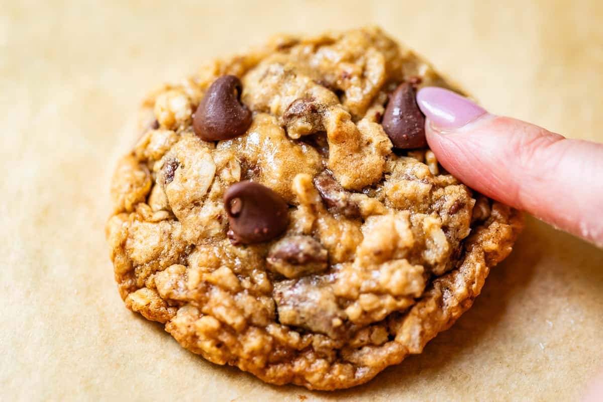 finger pushing a chocolate chip into a baked oatmeal chocolate chip cookie.