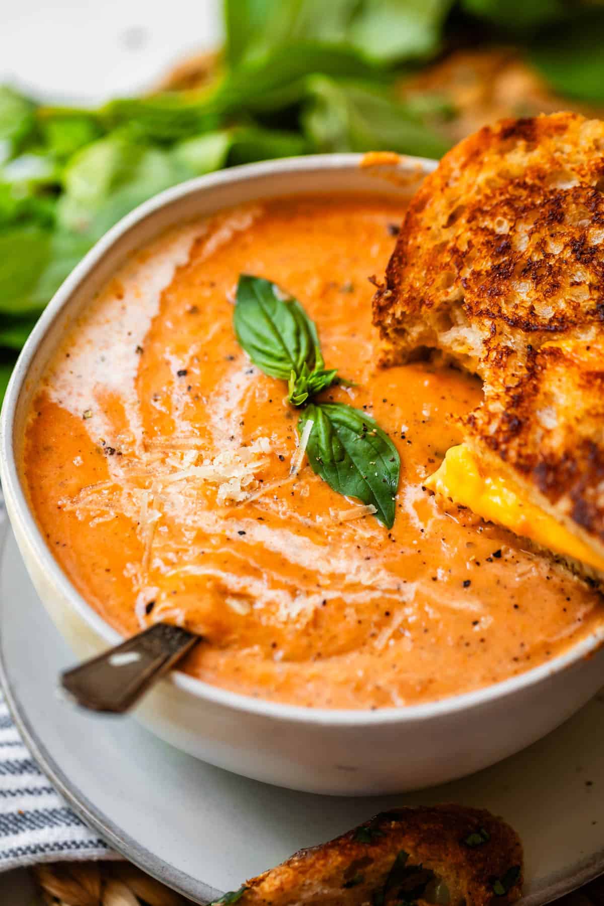 ceramic bowl of tomato bisque garnished with cream, basil, and grilled cheese.