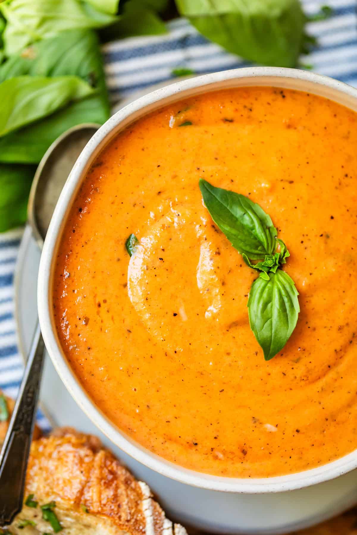 ceramic bowl of soup of tomato soup with basil garnish on table with spoon next to it.