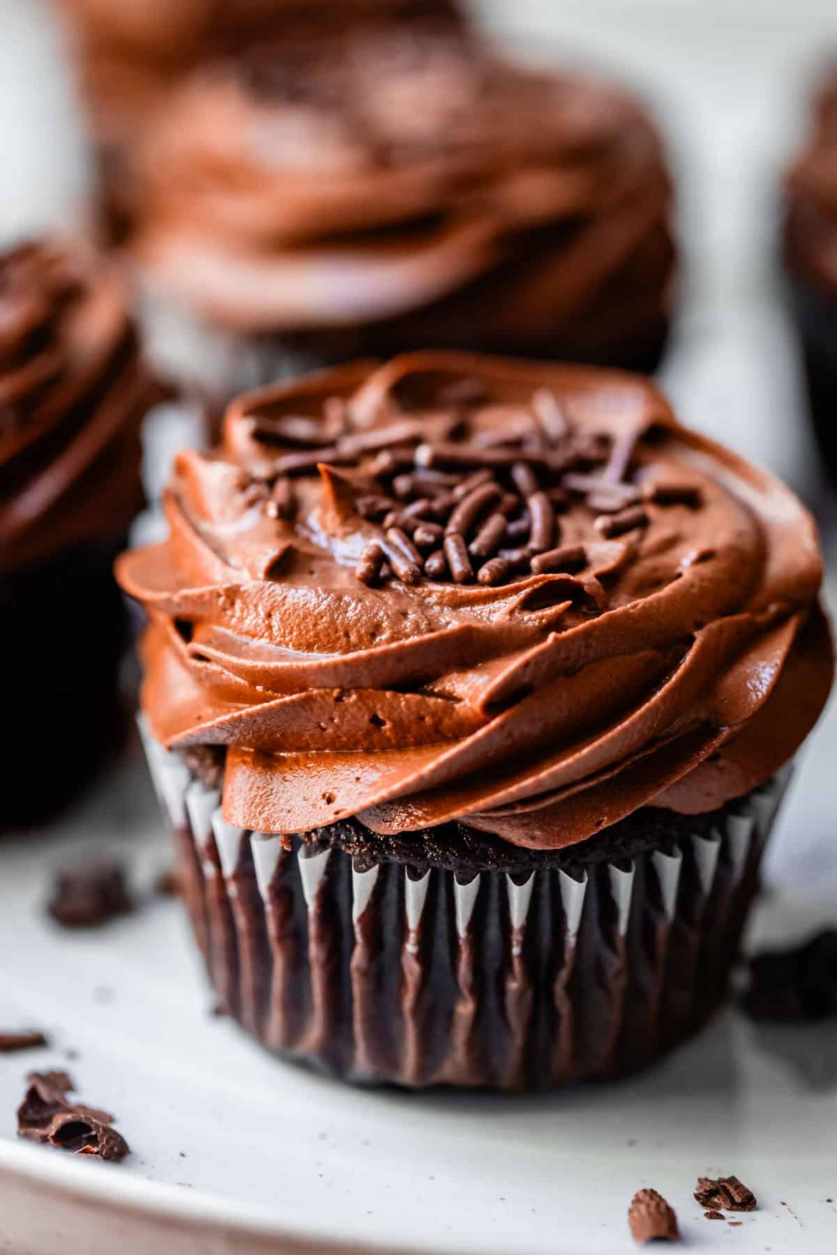 side view of a chocolate cupcake topped with piped chocolate frosting and sprinkles.