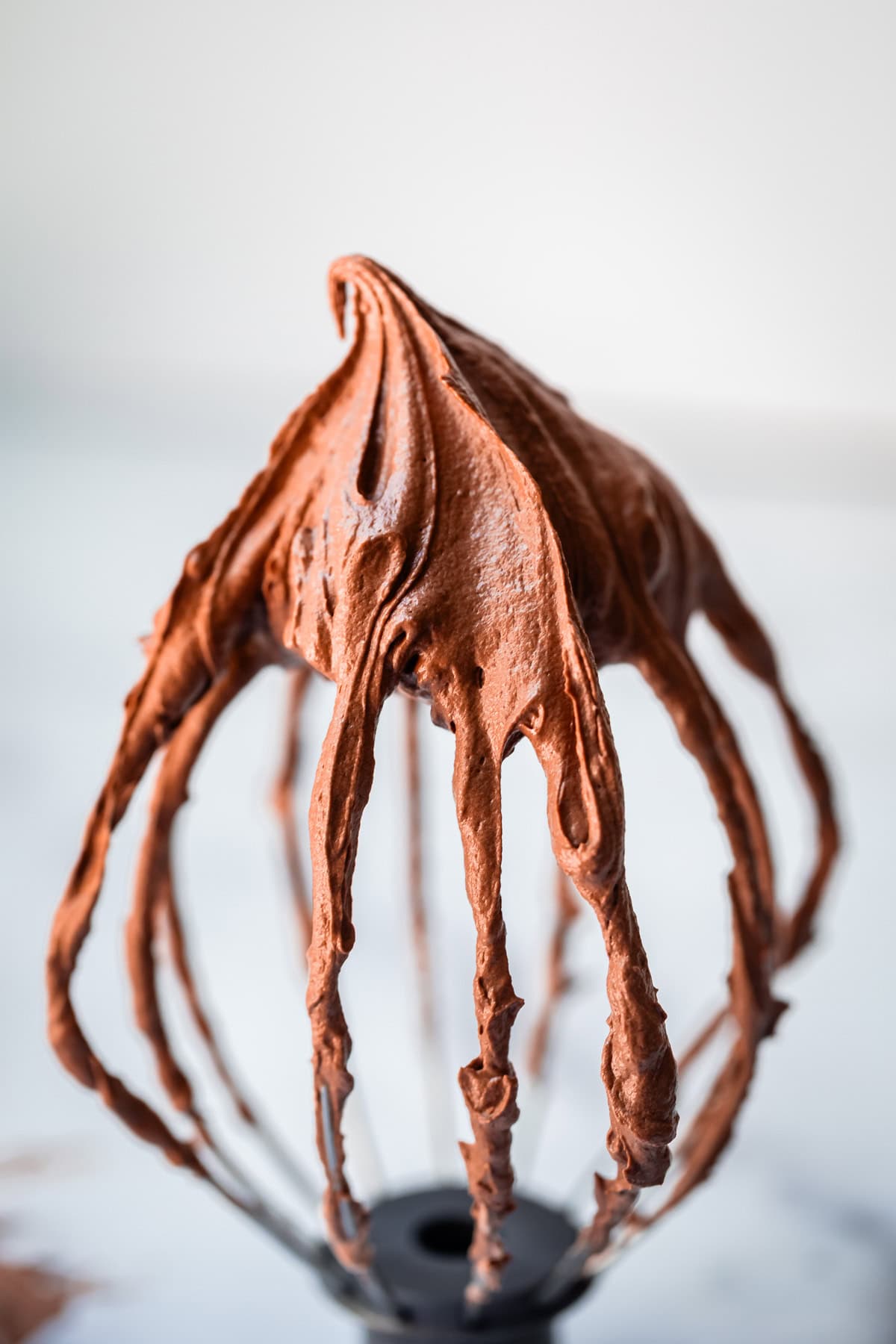 whisk attachment being held upside down with chocolate frosting on the end at a peak.