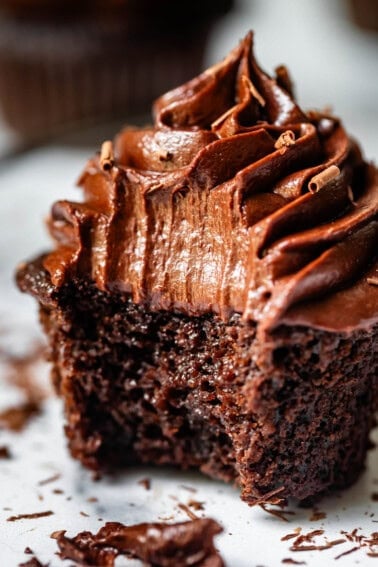 chocolate cupcake topped with piped chocolate frosting with a huge bite take from it.