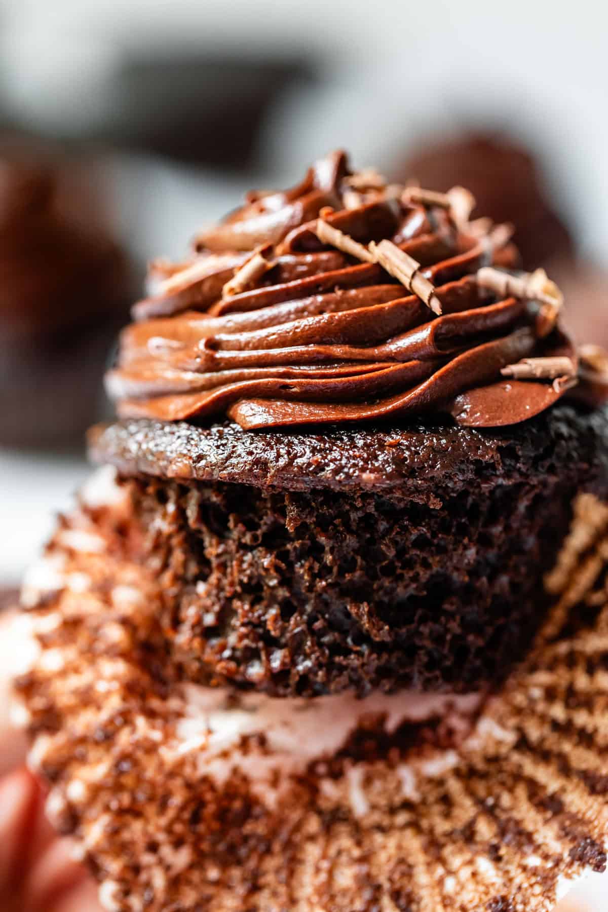 chocolate cupcake with piped chocolate frosting, liner pulled away to show cake.
