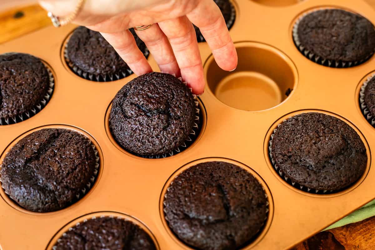hand lifting a baked chocolate cupcake out of a muffin tin.