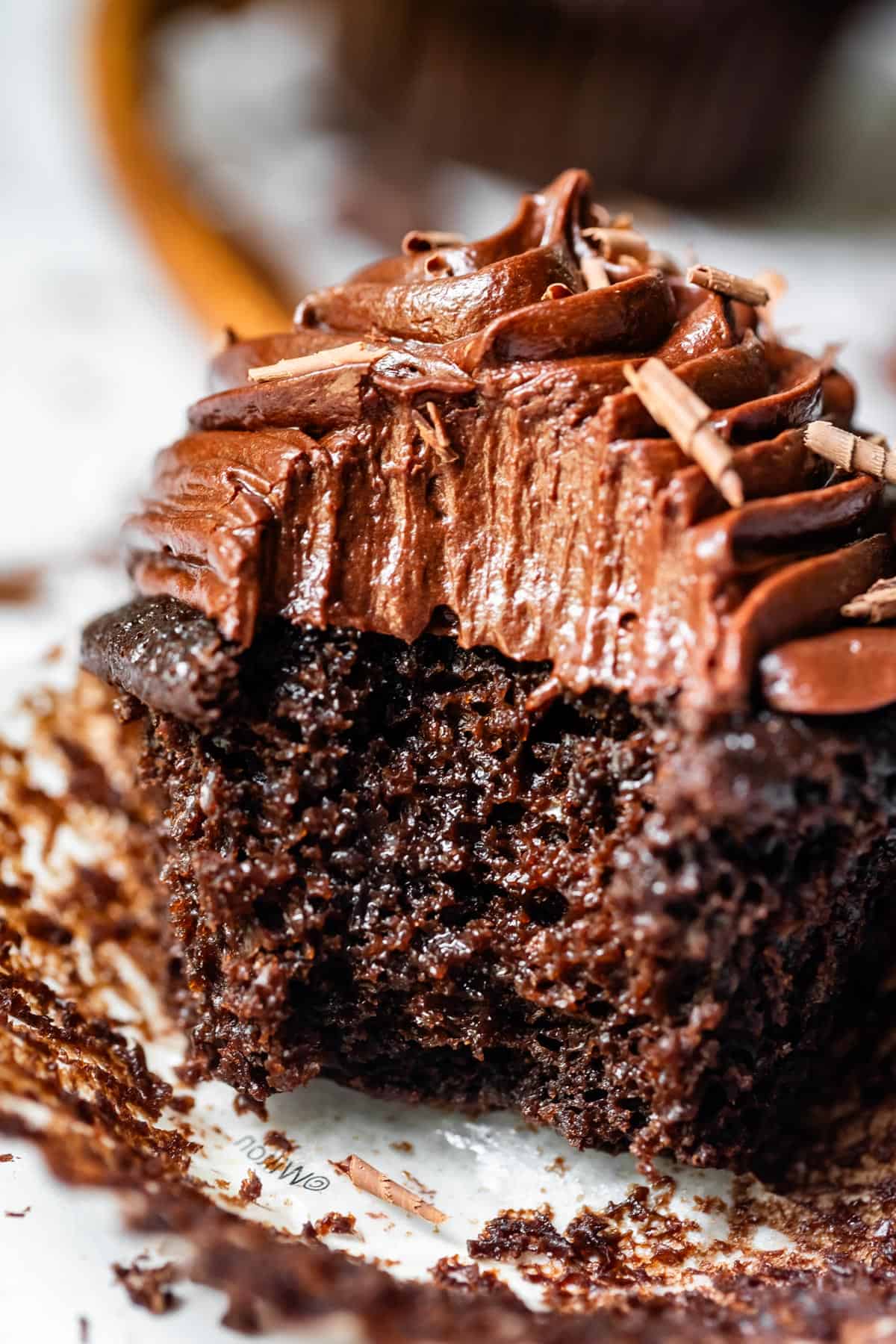 chocolate cupcake topped with piped chocolate frosting with a huge bite take from it.