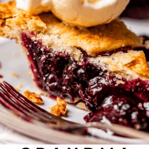 A slice of blackberry pie with a golden crust and rich berry filling, topped with a scoop of vanilla ice cream, on a plate. Text at the bottom reads Grandma Georgia’s Blackberry Pie - The Food Charlatan.