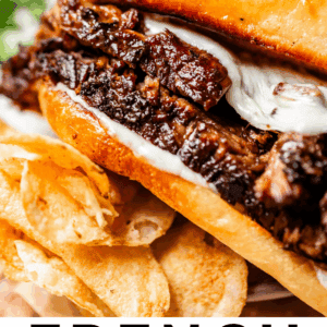 A close-up of a French dip sandwich filled with juicy beef and melted cheese, served with potato chips and a cup of au jus for dipping. Text reads: French Dip Sandwiches That’ll Knock Your Socks Off – The Food Charlatan.