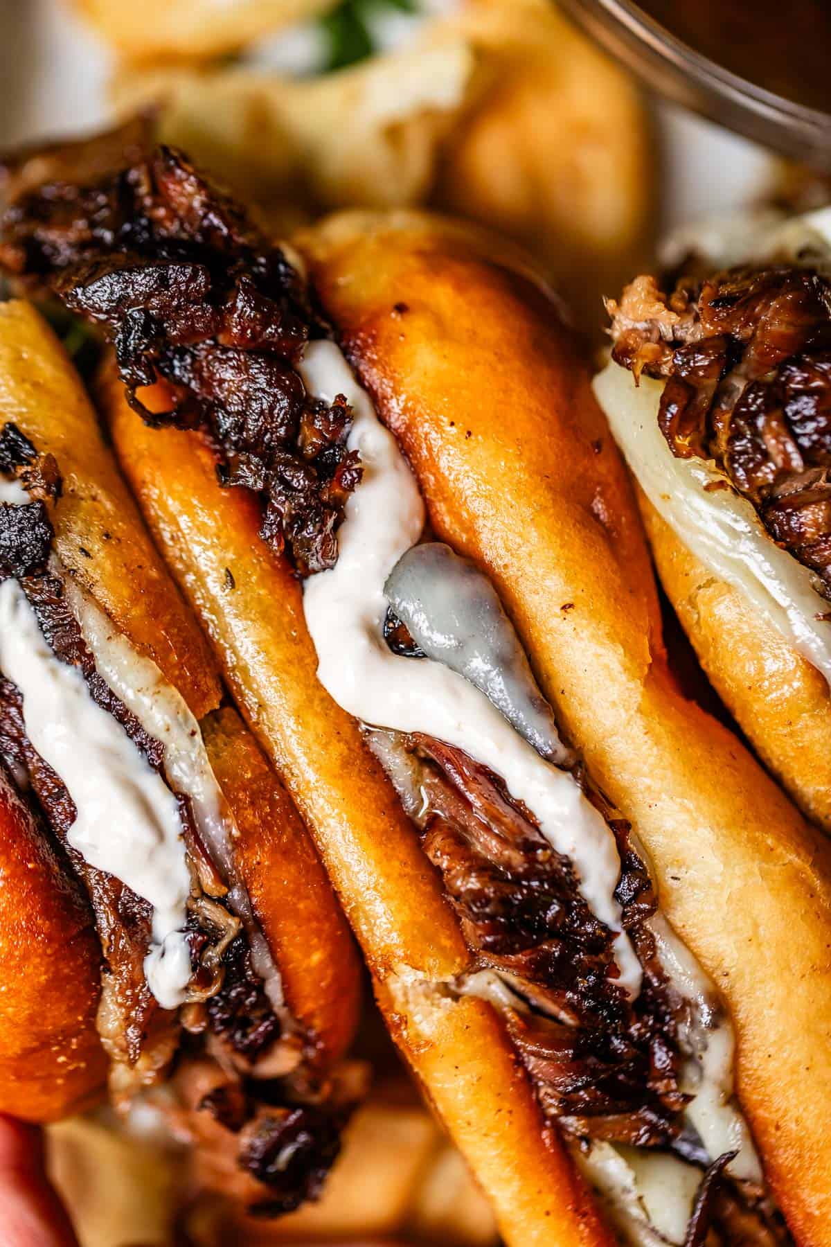 Close-up of a toasted sandwich filled with shredded beef, melted cheese, and a creamy white sauce. The bread is golden brown and slightly glossy, with tender meat and cheese visible inside.
