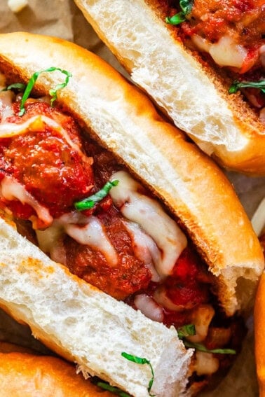 Meatball sub on parchment paper with meatballs, marinara, and garnishes of melted mozzarella and parsley.