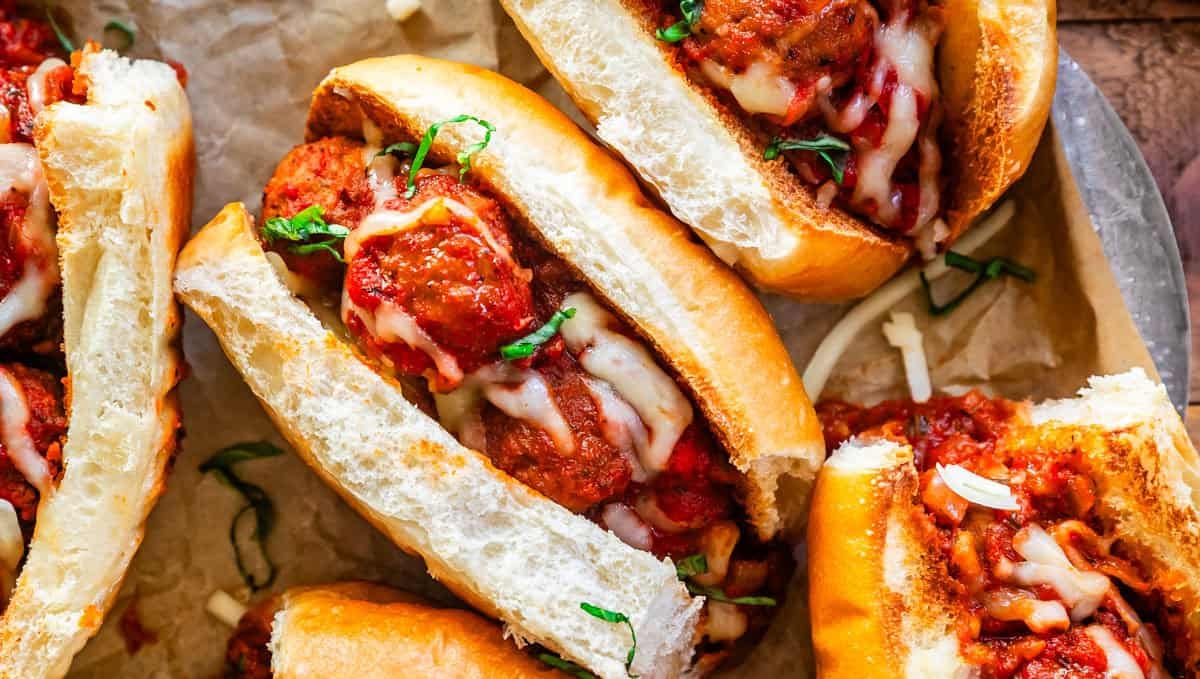 Meatball sub on parchment paper with meatballs, marinara, and garnishes of melted mozzarella and parsley.