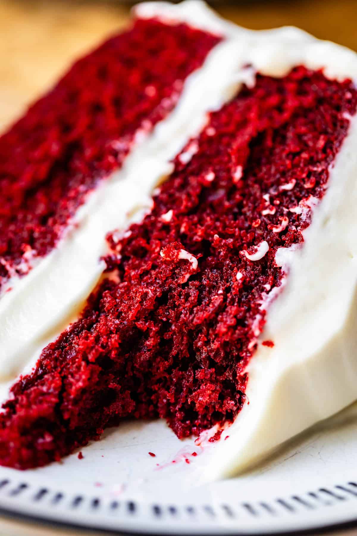 slice of red velvet cake with cream cheese frosting with a bite taken from it.