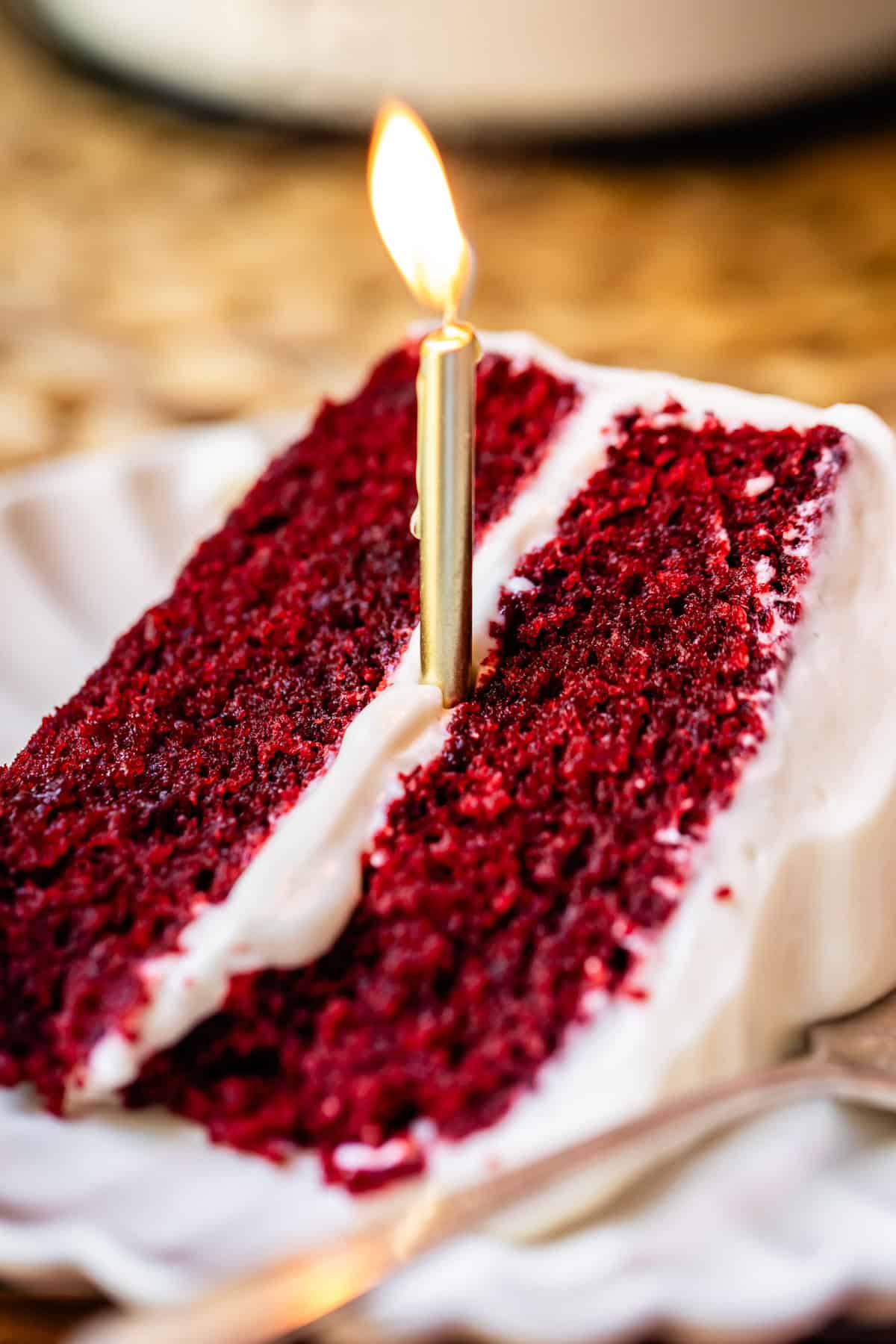 slice of red velvet cake with cream cheese frosting with a lit candle in it.