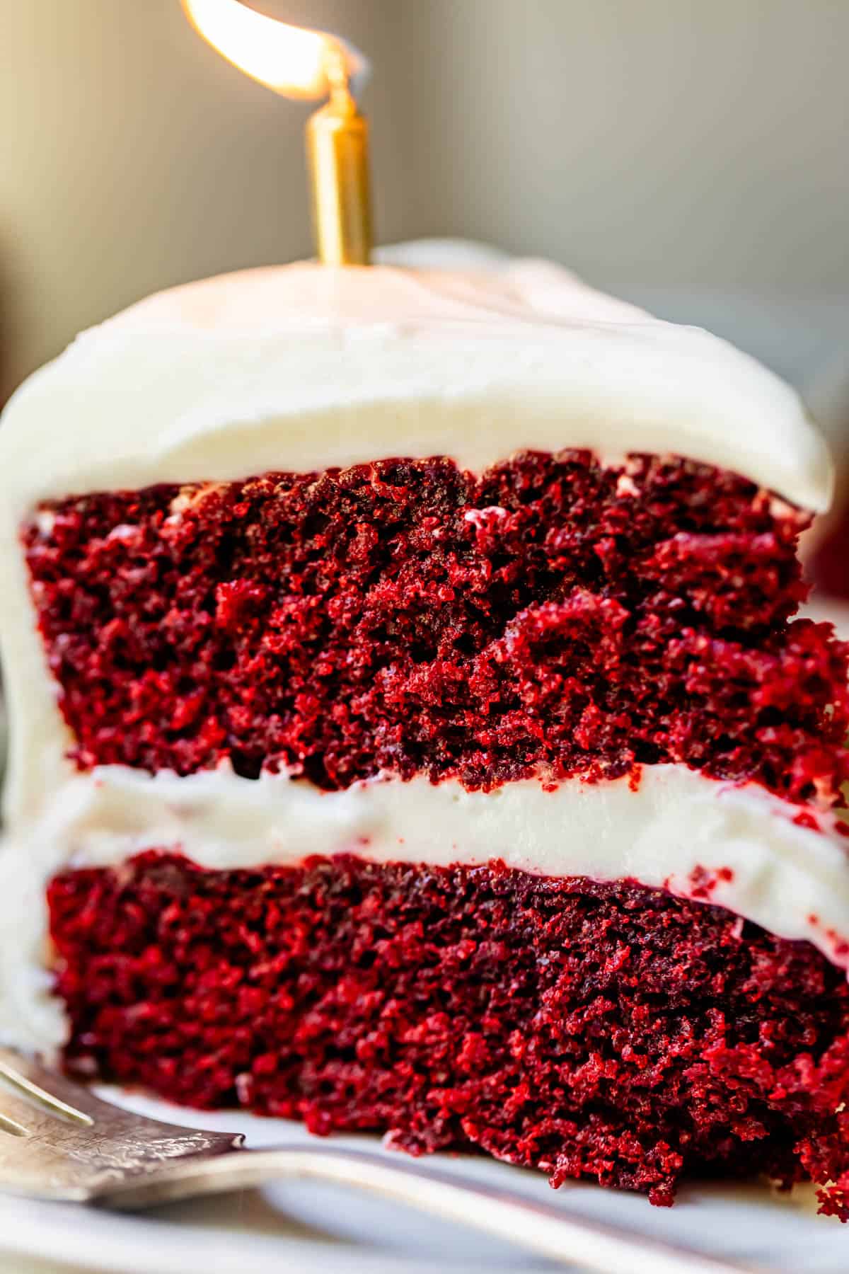 slice of red velvet cake with cream cheese frosting with a lit candle in it.