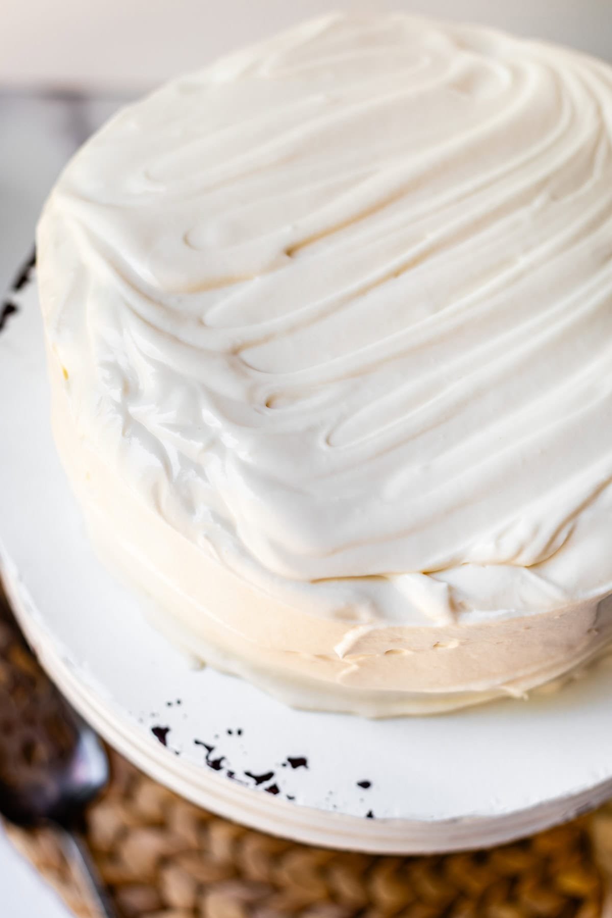 looking down at a whole cake frosting with whipped cream cream cheese frosting on a platter.