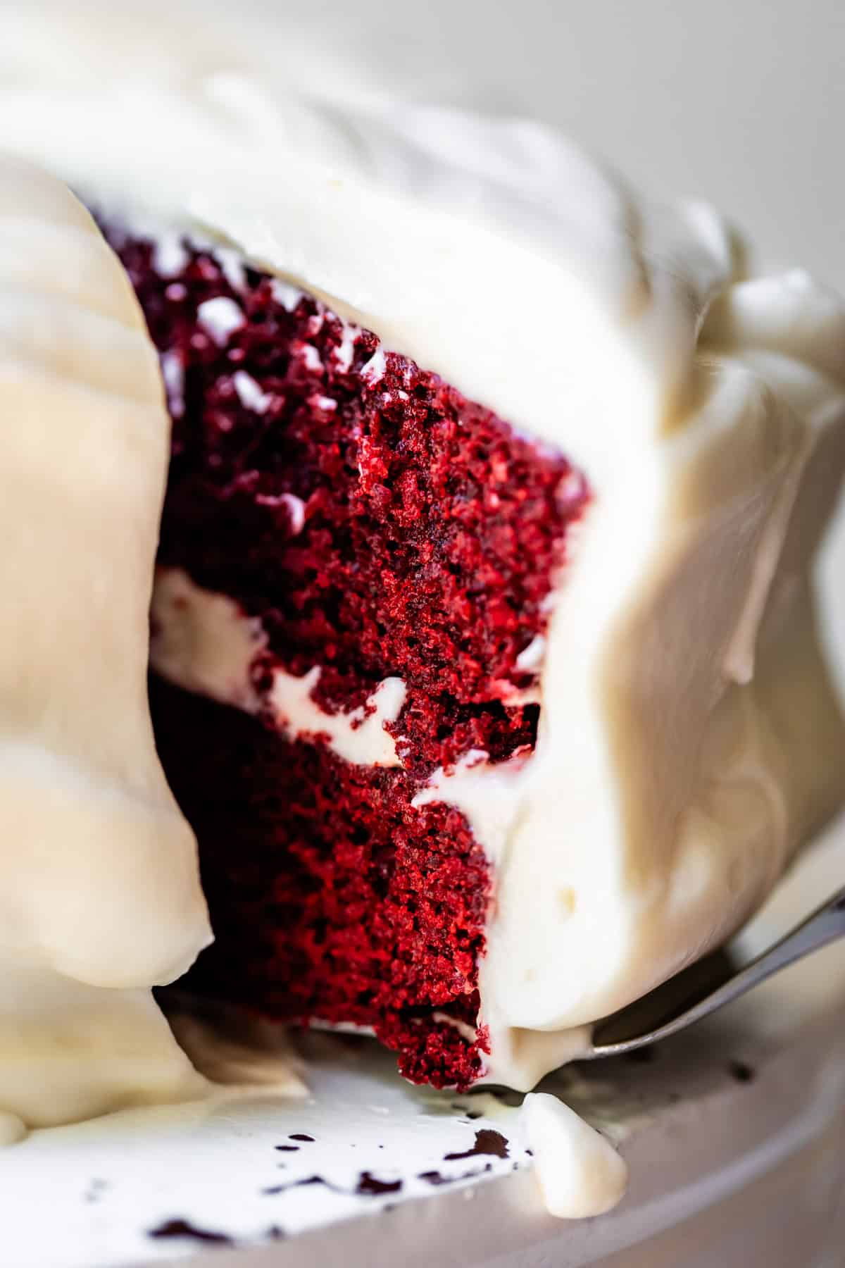 a cake server lifting up a piece of red velvet cake from the whole cake.