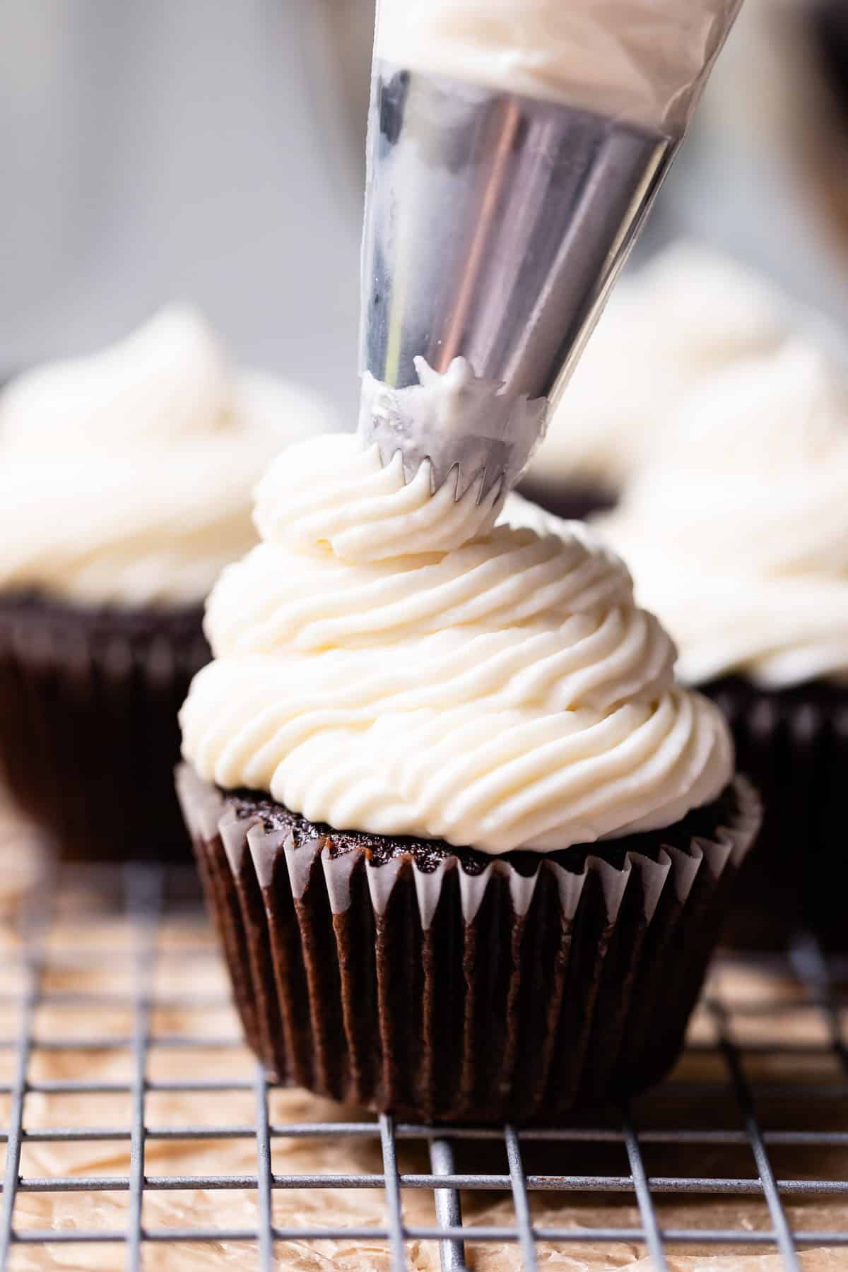 piping cream cheese frosting onto a chocolate cupcake.