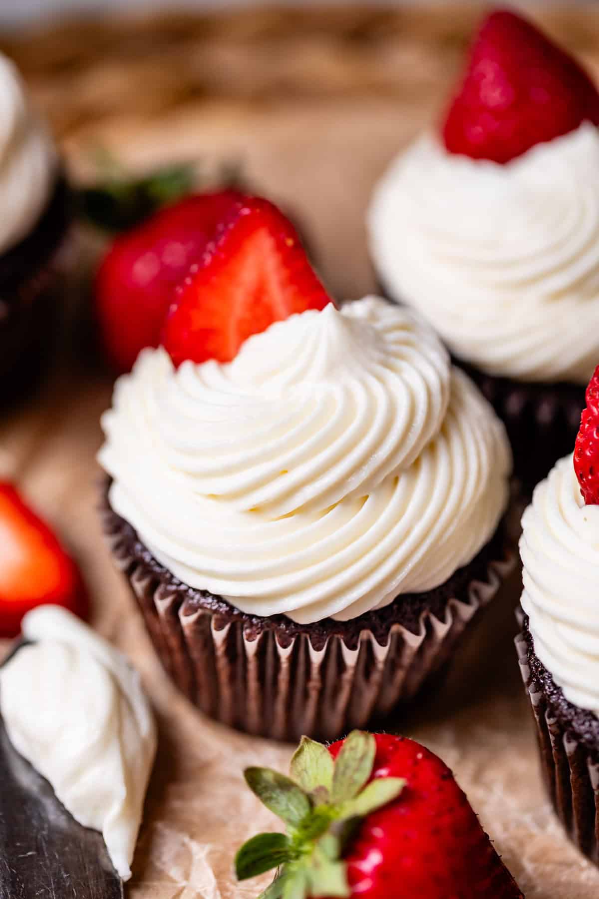 chocolate cupcakes on parchment paper topped with cream cheese frosting and strawberries.