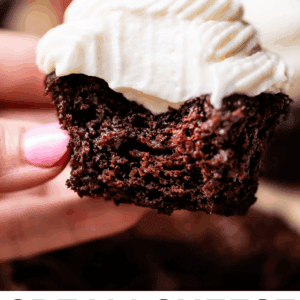 hand holding a chocolate cupcake with whipped cream cheese frosting and a strawberry.