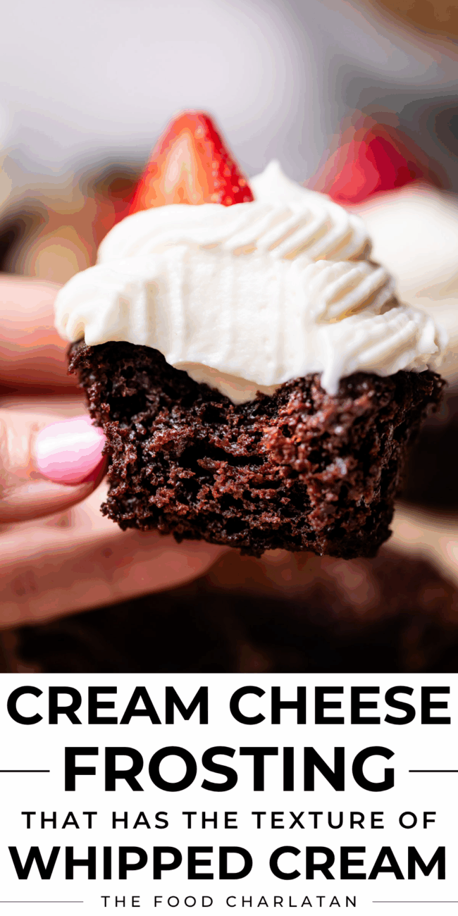 hand holding a chocolate cupcake with whipped cream cheese frosting and a strawberry.