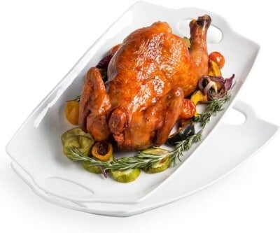 A whole roasted chicken served on a white rectangular platter, garnished with roasted vegetables.