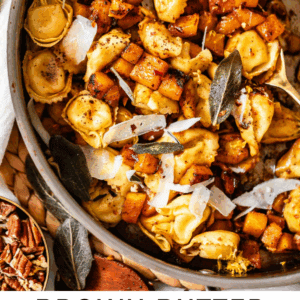 A skillet filled with tortellini, roasted butternut squash cubes, sage leaves, and shaved parmesan, displayed on a woven mat. Text overlay reads: Brown Butter Tortellini with Butternut Squash.