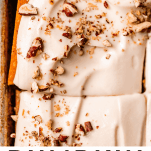 Close-up of a pumpkin cake topped with smooth maple cream cheese frosting and chopped pecans, with a spatula lifting a slice from the pan. Text at the bottom reads: Pumpkin Cake Maple Cream Cheese Frosting The Food Charlatan.