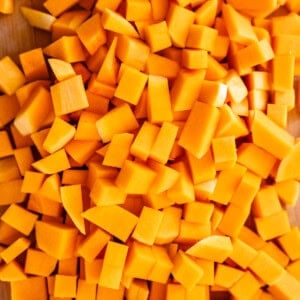 A pile of fresh, evenly diced orange butternut squash pieces spread out on a wooden cutting board.