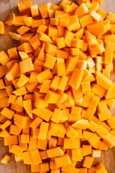 A pile of fresh, evenly diced orange butternut squash pieces spread out on a wooden cutting board.