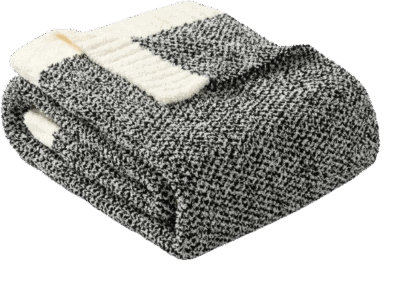 A folded black and white knitted blanket with a textured pattern and a cream-colored edge, placed on a plain white background.