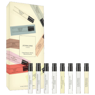 A Jo Malone London Cologne Discovery Collection gift box is shown with eight sample-sized cologne spray bottles arranged in front, each featuring a different fragrance. The box displays pastel-colored labels for each scent.