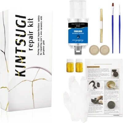 Kimtsugi repair kit with box, resin, gold powder, paintbrushes, spatula, gloves, two small jars, and an instruction sheet arranged neatly on a white background.