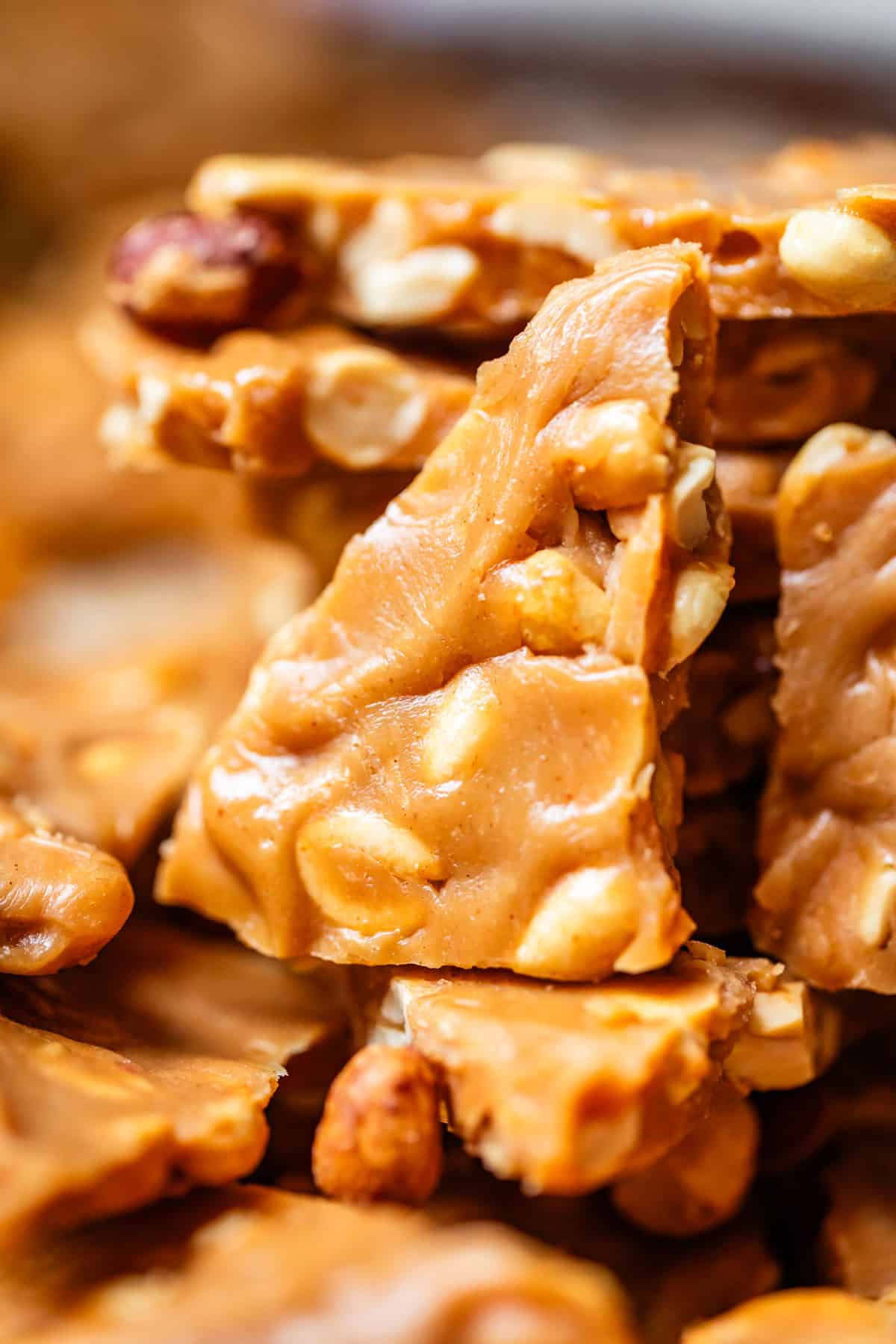 Close-up of pieces of peanut brittle, showing golden, glossy caramel broken into jagged shards with whole peanuts embedded throughout.