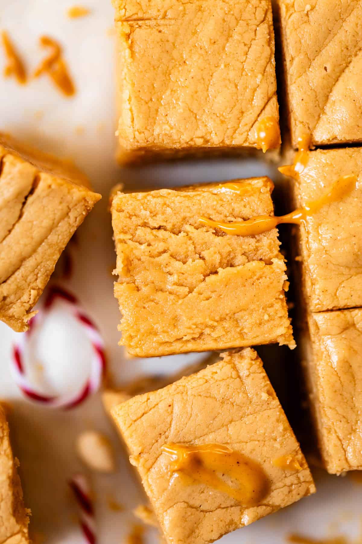 Close-up of creamy peanut butter fudge squares on a white surface, with a small piece of red and white striped candy cane in the corner. Some fudge pieces are slightly smeared with peanut butter.
