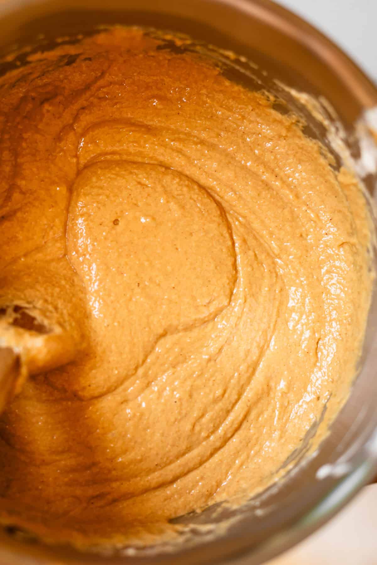 Thick, creamy, light brown batter being mixed in a metal bowl with a wooden spoon, likely for baking bread or cake.
