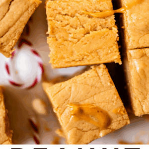 Close-up of creamy, golden peanut butter fudge squares arranged on parchment paper, with a glimpse of a red and white candy cane nearby. Text at the bottom reads: Peanut Butter Fudge: The Food Charlatan.