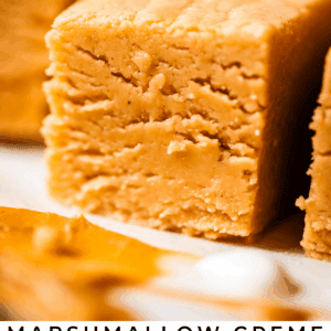 Close-up of creamy, golden peanut butter fudge squares with a smooth texture. Text overlay reads: Marshmallow Creme Peanut Butter Fudge - The Food Charlatan.