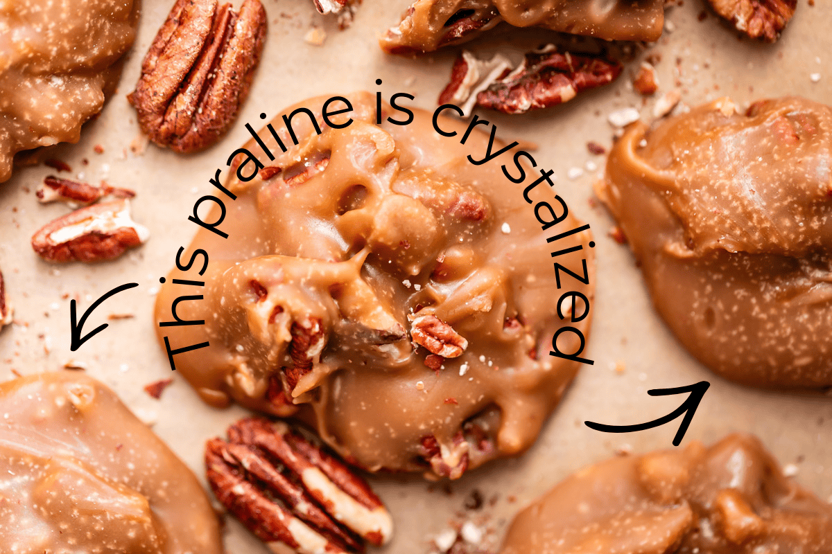 Close-up of several pecan pralines on parchment paper, with text and arrows pointing to one praline that reads, This praline is crystalized.