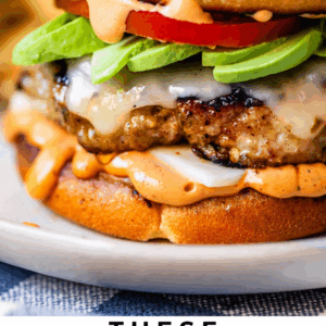 Close-up of a juicy turkey burger with lettuce, tomato, avocado, cheese, and sauce on a toasted bun. Text below reads: “These turkey burgers are legit. The Food Charlatan.”.